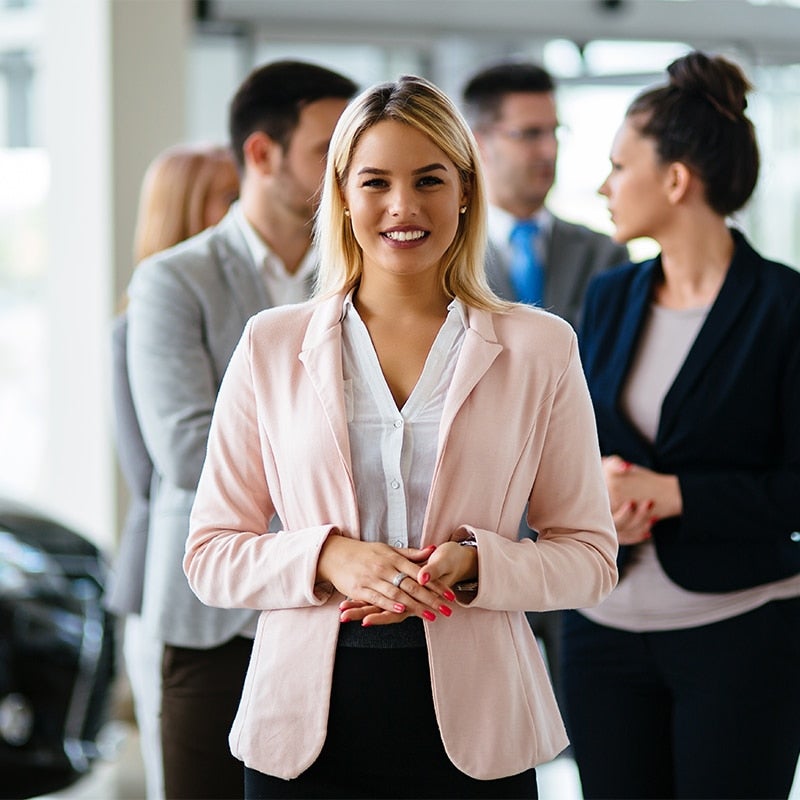A sales team stands smiling, ready to help a couple who are shopping for a new vehicle in a GMC sales center..